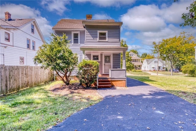 traditional style home with a chimney, covered porch, a front lawn, and fence