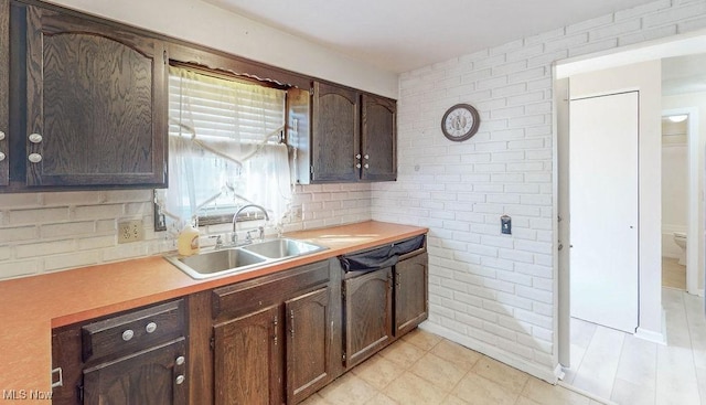 kitchen featuring a sink, dark brown cabinetry, brick wall, and light countertops