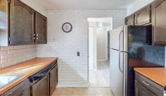 kitchen with brick wall, dark brown cabinetry, light countertops, freestanding refrigerator, and a sink