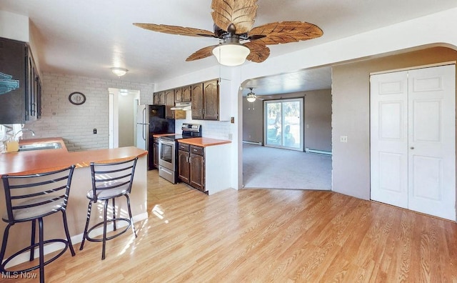 kitchen featuring light wood-type flooring, a sink, a baseboard heating unit, a kitchen breakfast bar, and appliances with stainless steel finishes