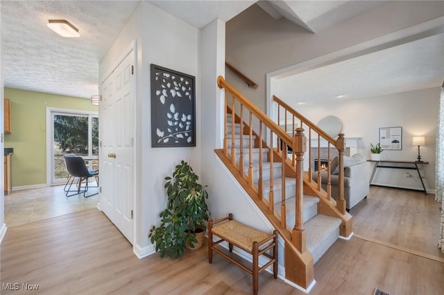 stairway featuring a textured ceiling, baseboards, and wood finished floors