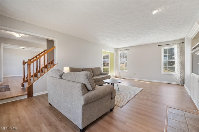 living room with stairs, light wood-style flooring, baseboards, and a textured ceiling