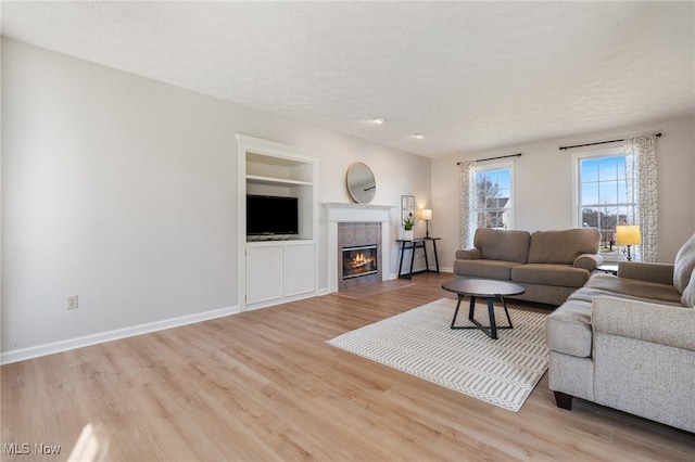 living room with built in shelves, baseboards, a fireplace, light wood-style floors, and a textured ceiling