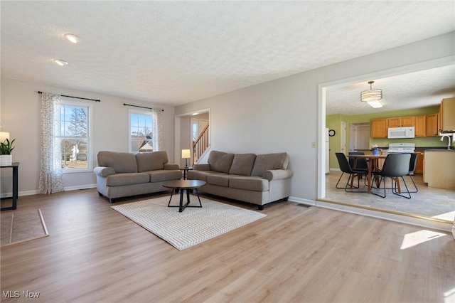 living room with stairway, light wood-style floors, baseboards, and a textured ceiling