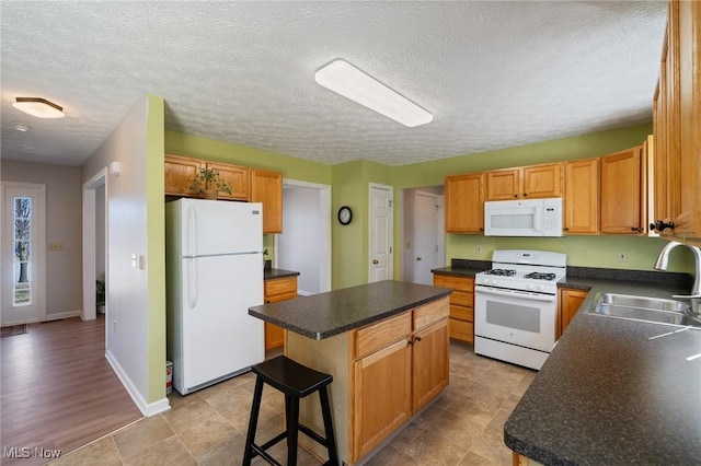 kitchen with a sink, white appliances, a kitchen island, and dark countertops