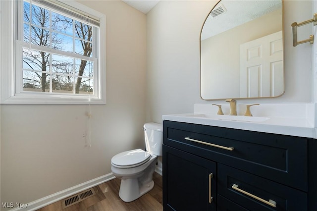 half bathroom featuring visible vents, baseboards, toilet, and wood finished floors