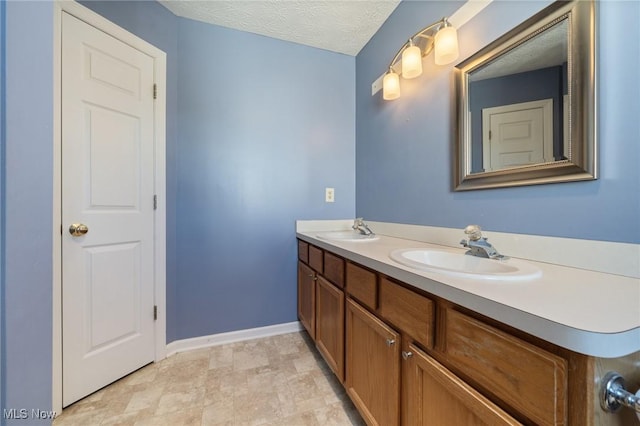 bathroom featuring double vanity, a textured ceiling, baseboards, and a sink