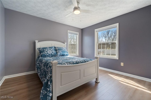 bedroom featuring baseboards, dark wood-type flooring, a ceiling fan, and a textured ceiling