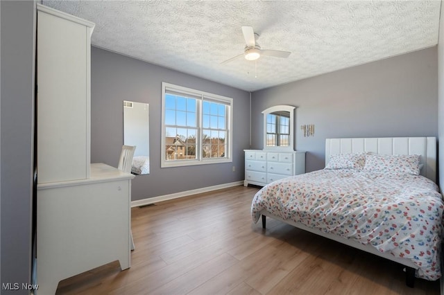 bedroom featuring visible vents, a textured ceiling, wood finished floors, baseboards, and ceiling fan