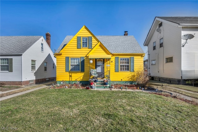 bungalow-style home with a chimney, entry steps, a shingled roof, and a front yard