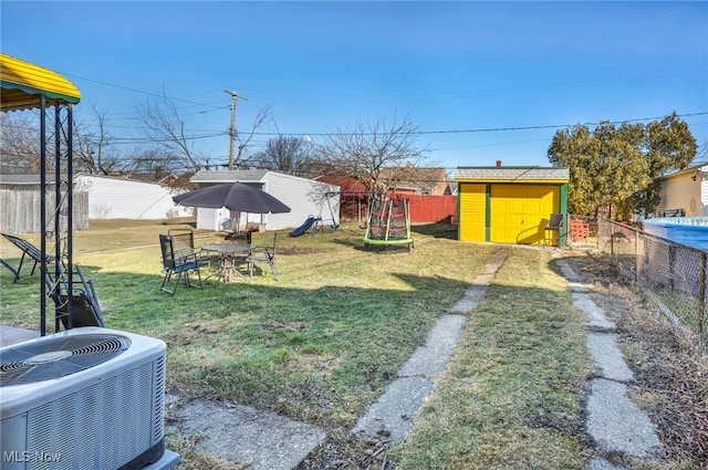 view of yard with fence, a playground, a storage shed, an outdoor structure, and central AC unit