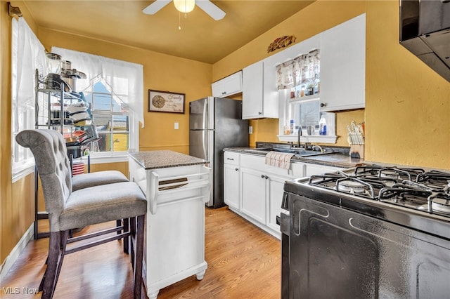 kitchen featuring dark countertops, white cabinetry, freestanding refrigerator, light wood finished floors, and gas range