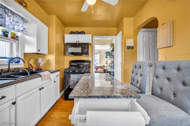 kitchen with light wood finished floors, black appliances, arched walkways, white cabinetry, and a sink