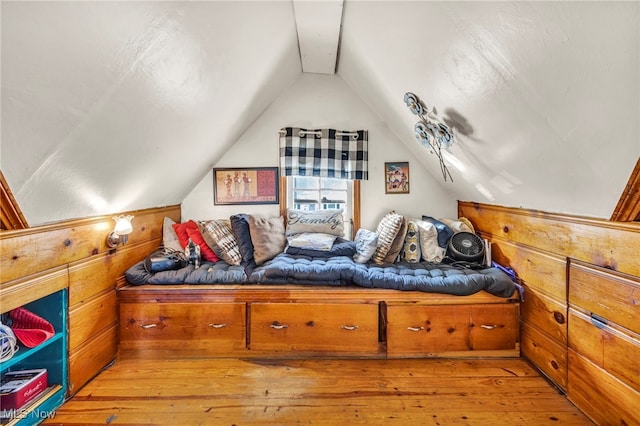 bedroom with wood walls, light wood-type flooring, and vaulted ceiling