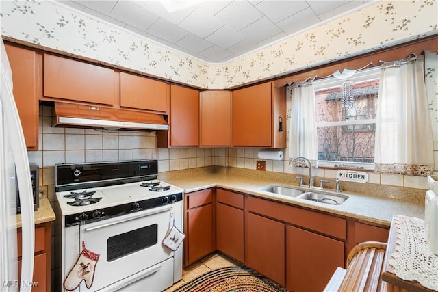 kitchen with light countertops, white gas range oven, under cabinet range hood, and a sink