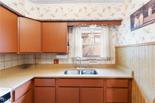 kitchen with stove, wallpapered walls, light countertops, and a sink