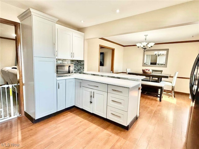 kitchen featuring stainless steel microwave, light wood-style flooring, a peninsula, and light countertops