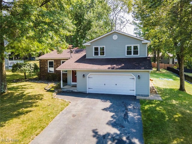 tri-level home with a front yard, fence, a garage, and aphalt driveway