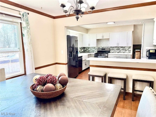 kitchen with black appliances, tasteful backsplash, light wood-style floors, an inviting chandelier, and light countertops