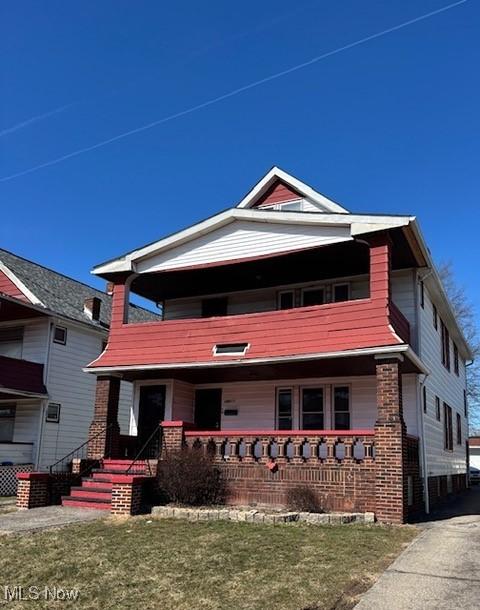 view of front of property with brick siding, a balcony, a porch, and a front lawn