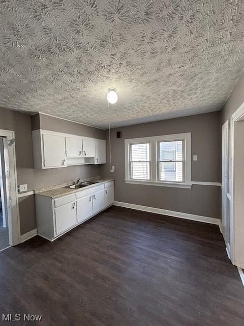 kitchen featuring baseboards, a sink, dark wood-type flooring, light countertops, and white cabinetry