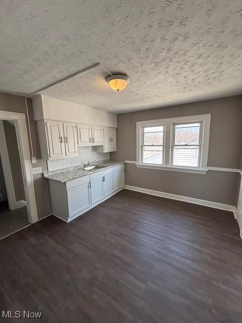 kitchen featuring baseboards, dark wood finished floors, a sink, decorative backsplash, and a textured ceiling