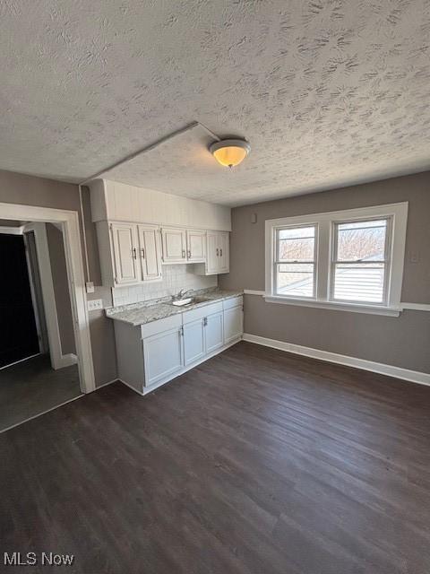 kitchen featuring dark wood-style floors, white cabinetry, baseboards, and a sink