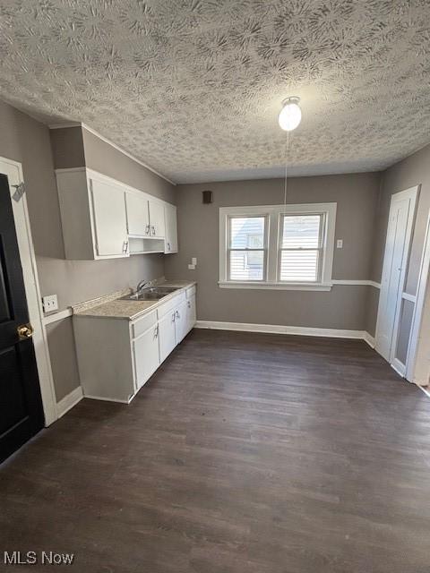 kitchen with baseboards, light countertops, dark wood-style floors, white cabinetry, and a sink