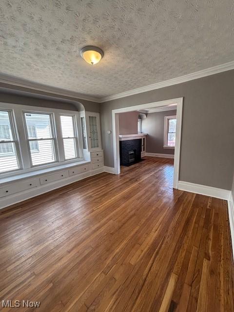 unfurnished living room with a textured ceiling, crown molding, baseboards, and wood finished floors