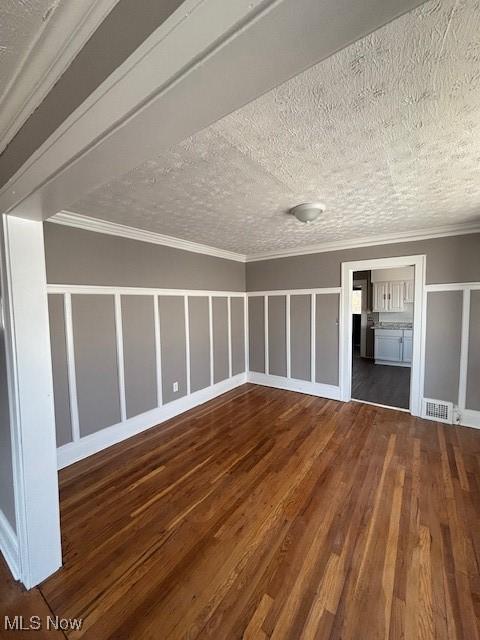 interior space featuring a textured ceiling, wood finished floors, visible vents, and ornamental molding