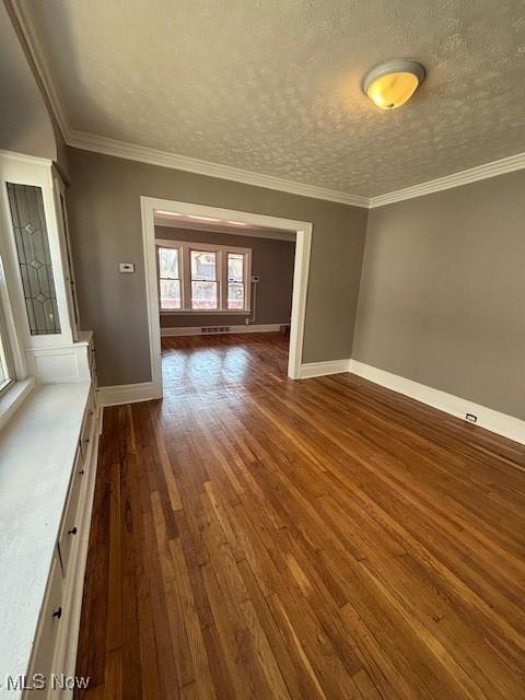 spare room featuring a textured ceiling, dark wood-style floors, baseboards, and ornamental molding