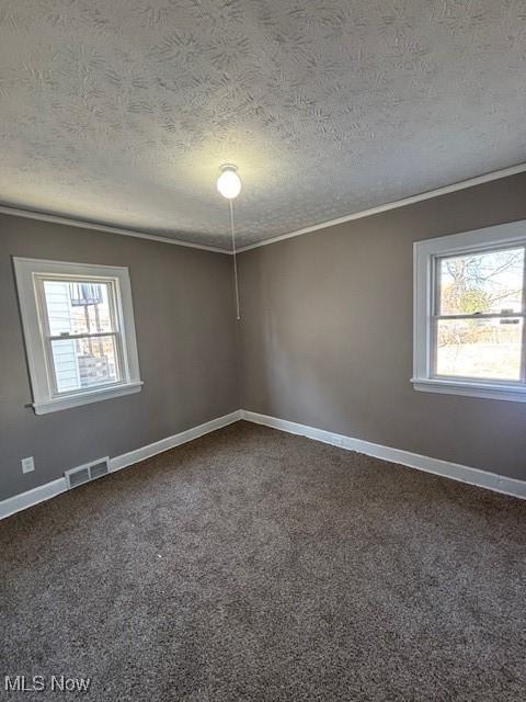 unfurnished room with crown molding, plenty of natural light, visible vents, and dark colored carpet