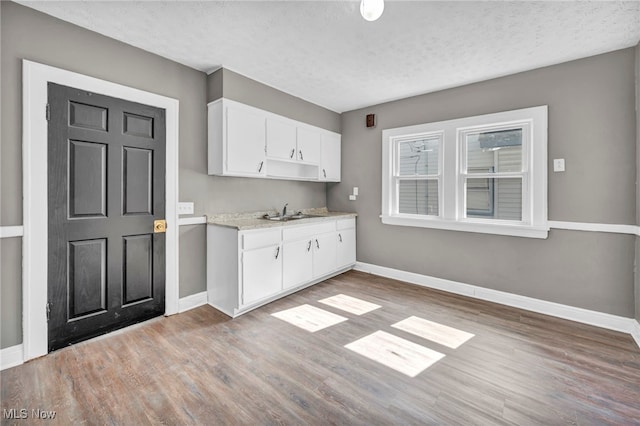 12117 Craven Ave, Cleveland, OH 44105 - kitchen with baseboards, light wood finished floors, white cabinetry, a sink, and a textured ceiling