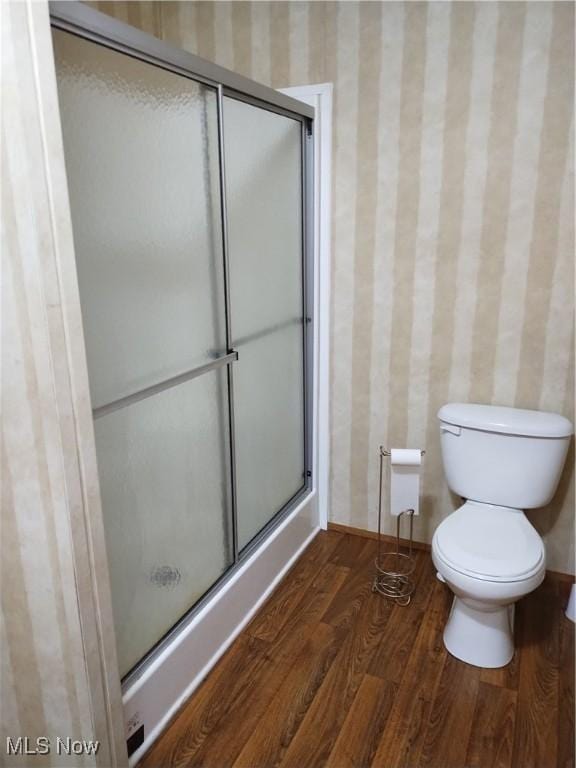 full bath featuring a shower with door, toilet, and wood finished floors