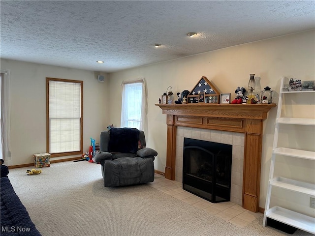 living area with a tiled fireplace, light colored carpet, baseboards, and a textured ceiling