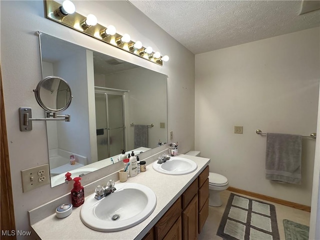 bathroom with a textured ceiling, a shower stall, double vanity, and a sink