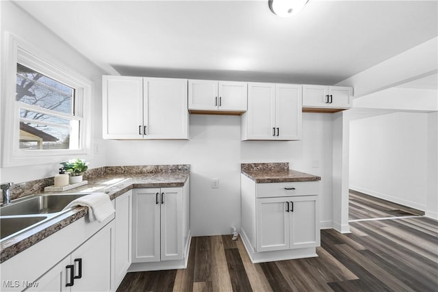 kitchen featuring dark countertops, white cabinets, dark wood-style flooring, and a sink