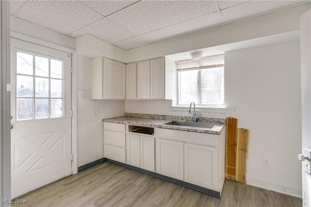 kitchen featuring a sink, a drop ceiling, white cabinets, and light wood finished floors