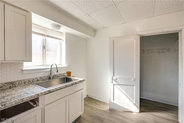 kitchen featuring light wood-style flooring, a sink, a drop ceiling, backsplash, and light countertops