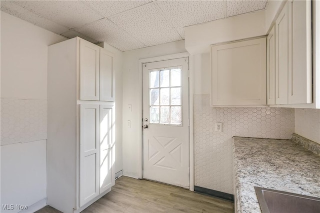 interior space with a drop ceiling, light wood-type flooring, and white cabinetry