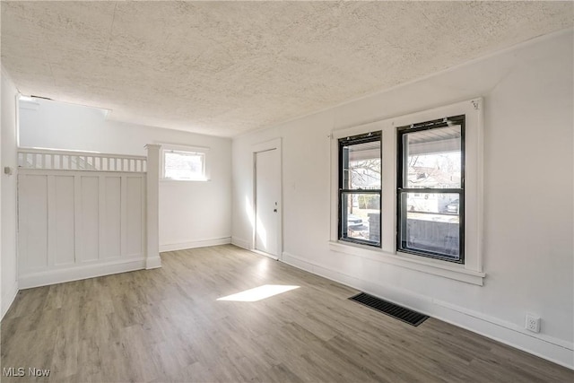 spare room with visible vents, a textured ceiling, baseboards, and wood finished floors