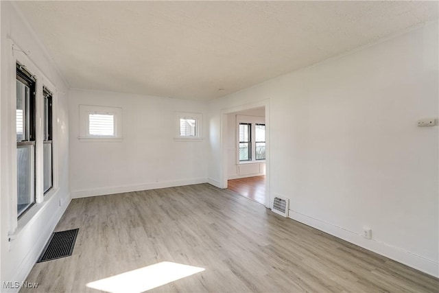 empty room with visible vents, a healthy amount of sunlight, and light wood finished floors