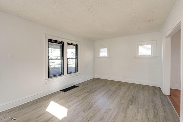 empty room with baseboards, wood finished floors, visible vents, and a textured ceiling