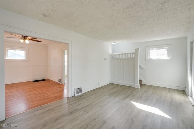 empty room with visible vents, a textured ceiling, wood finished floors, and stairs