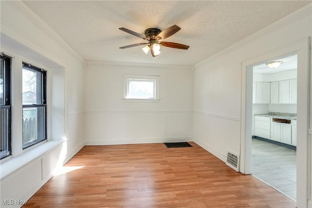 spare room featuring visible vents, light wood-style flooring, a textured ceiling, and ornamental molding