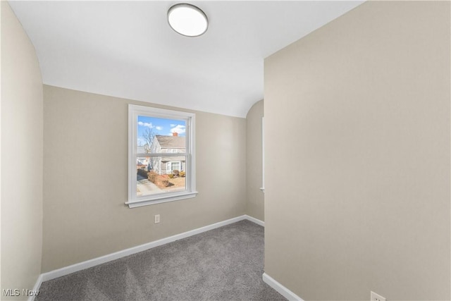 carpeted spare room featuring baseboards and lofted ceiling