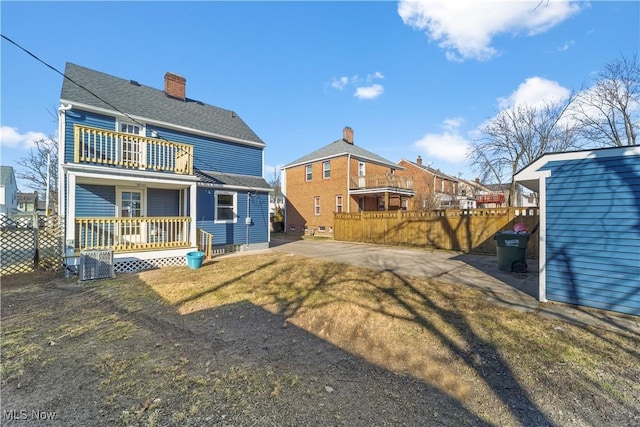 rear view of house with a chimney, an outdoor structure, a balcony, and fence