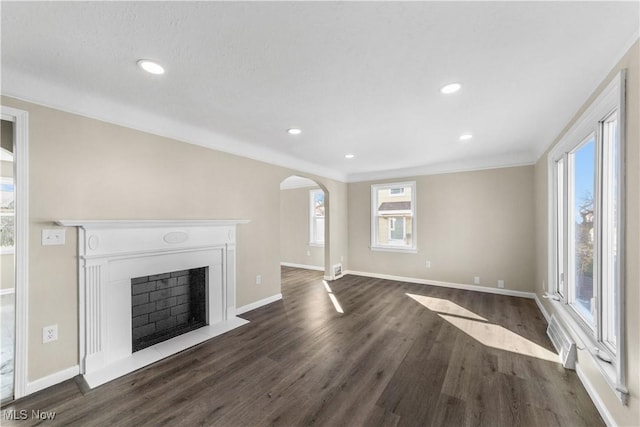 unfurnished living room featuring dark wood finished floors, a fireplace with flush hearth, baseboards, and arched walkways