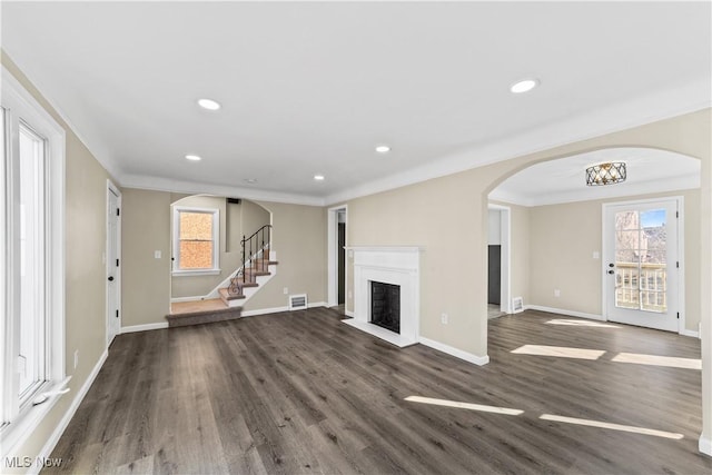 unfurnished living room with dark wood-style floors, arched walkways, a fireplace, baseboards, and stairs