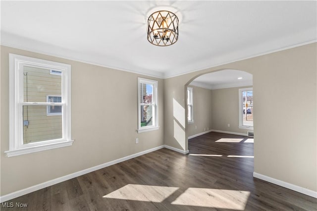 spare room with crown molding, baseboards, a chandelier, wood finished floors, and arched walkways